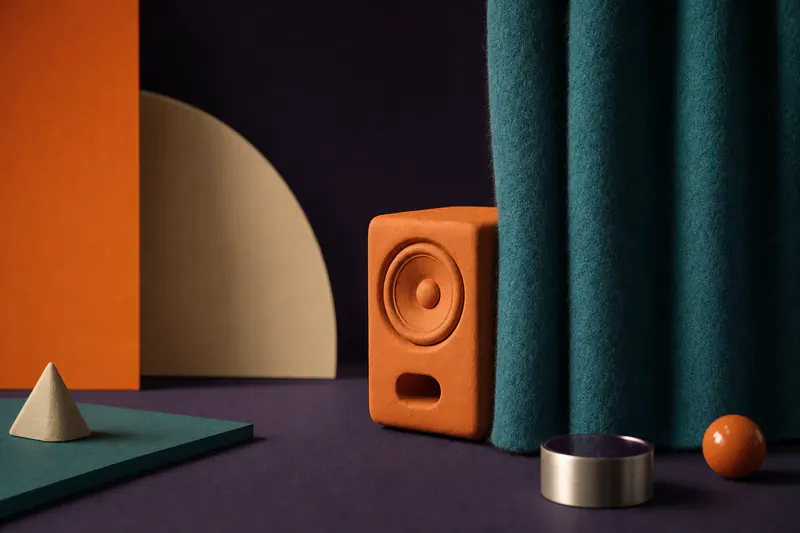 Illustration: a teal felt curtain half drawn in front of a small orange clay speaker on a violet field.