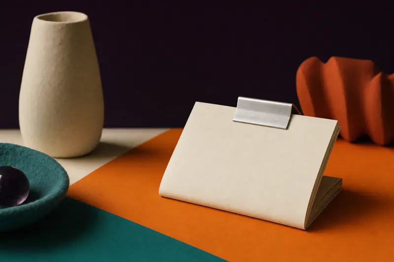 Illustration: a neatly folded cream paper document held by a brushed aluminium clip on an orange plane.